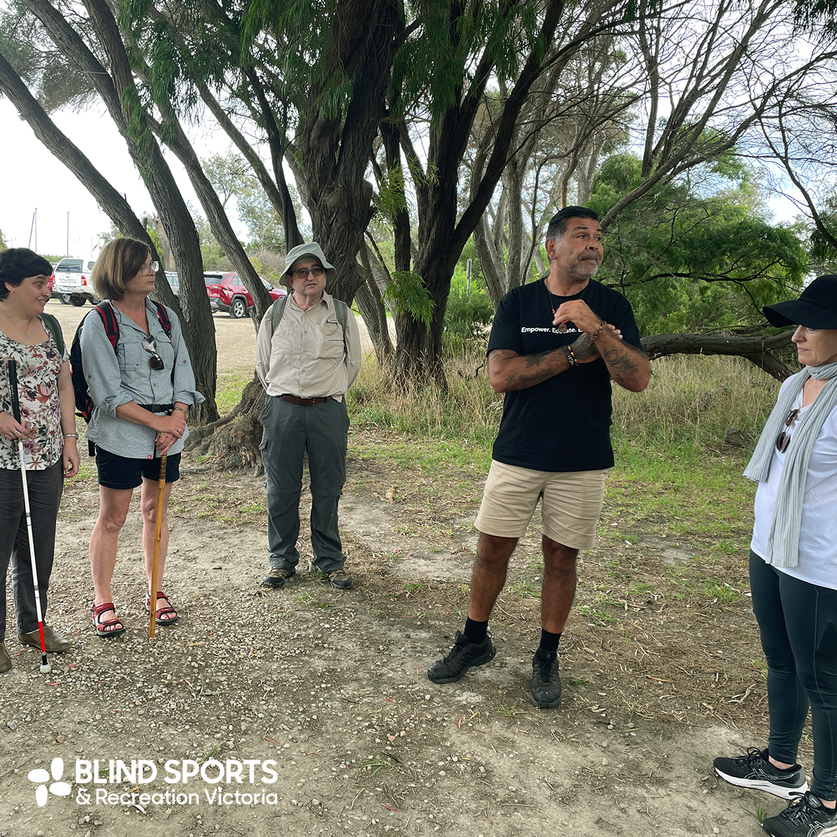 Lionel Lauch, an indigenous teacher,  standing in bushland talking to a group of participants from BSRV. 